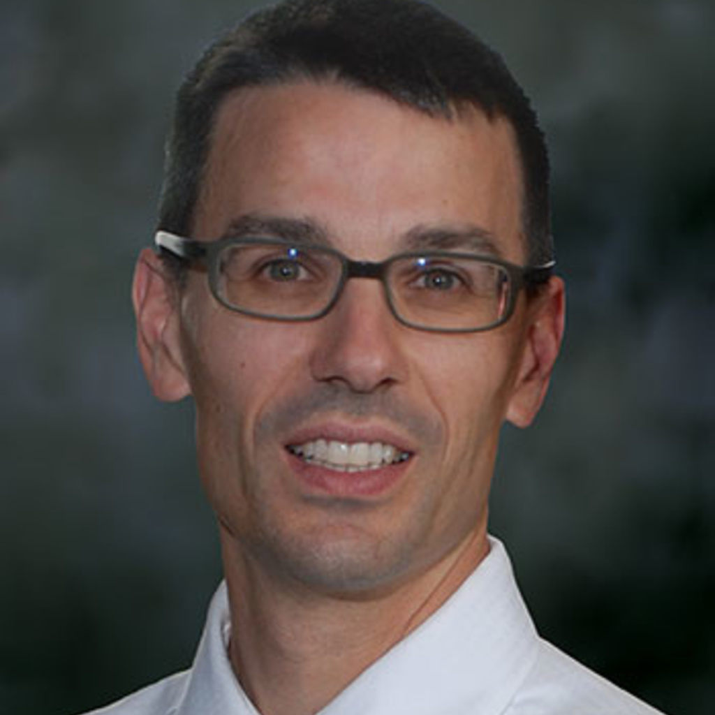 Photo of dark haired man in white shirt and tie with glasses