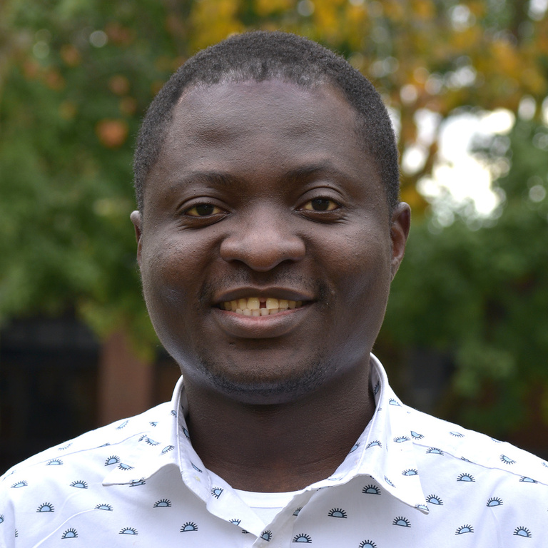 Male with dark features and warm smile in a light colored shirt