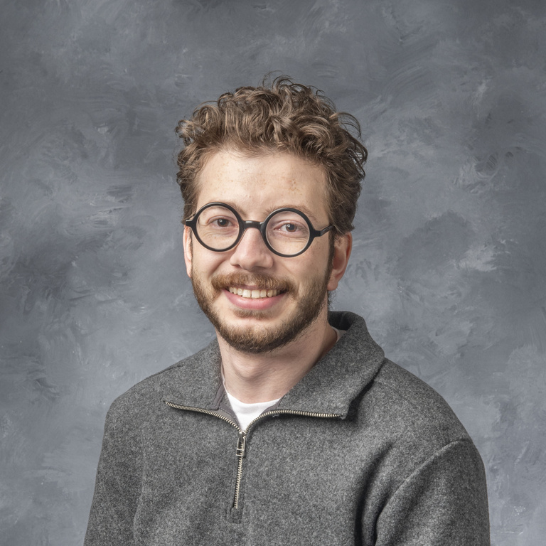 Photo of young man with curly brown hair and round glasses